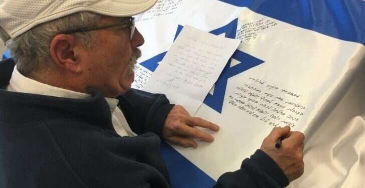 A man signs an Israeli flag at Ammunition Hill in Jerusalem Thousands of signed Israeli flags to enter Independence Day time capsule