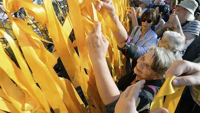 Participants place yellow ribbons with Jewish names on a barbed wire fence during Sunday's march March honors Warsaw's Jews, activist who warned of genocide