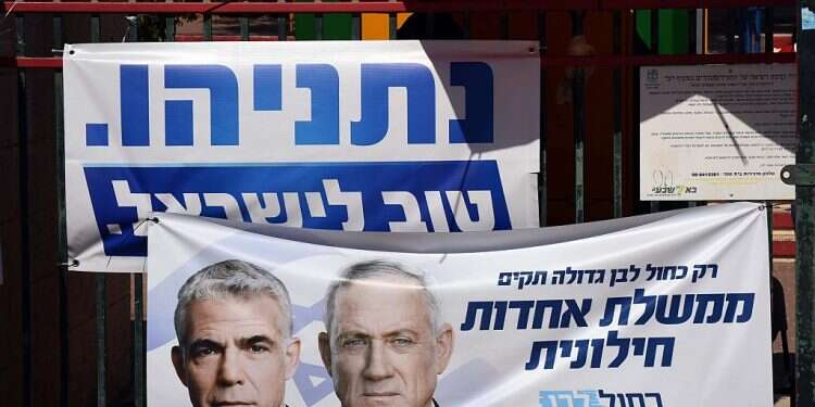 A campaign sign for Blue and White promising a 'secular unity government' hangs in front of a Likud banner Blue and White team ordered to 'drag out' talks until PM's hearing