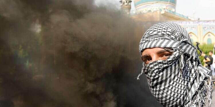 An Iraqi demonstrator next to smoke from burning tires during ongoing anti-government protests, in Baghdad, Sunday Iraqi protesters attack Iranian consulate in Karbala