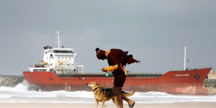 A man walks with his dog along the shore of the Mediterranean Sea as a cargo vessel that arrived at Israel's Ashdod Port and was swept away when a storm began is seen nearby, Dec. 26, 2019 Storm beaches merchant ship near southern Israeli port
