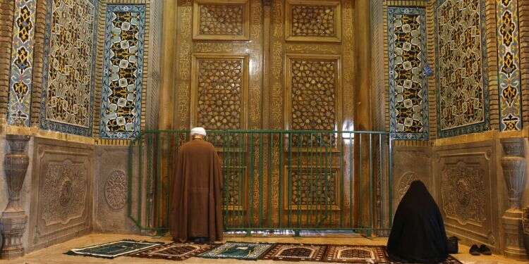 A cleric and a woman pray behind a closed door of Masoume shrine in the city of Qom, south of Tehran Hard-line Shiites storm Iran shrines closed over coronavirus