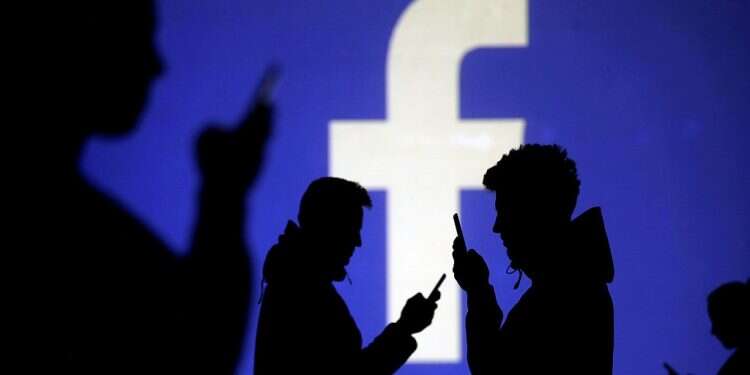 Silhouettes of mobile users are seen next to a screen projection of Facebook logo Facebook removes 2 Middle East-focused fake accounts