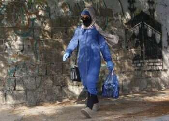 A Palestinian woman wearing a face mask carries her shopping bag during a lockdown imposed following the discovery of coronavirus cases Hamas says deal reached to calm violence with Israel