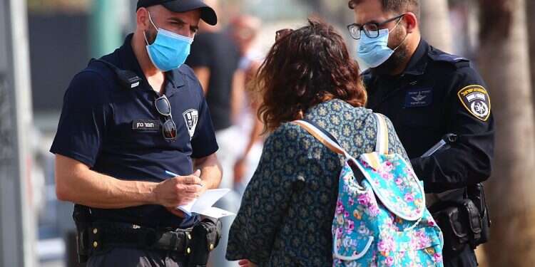 A police officer issues a fine to a woman for not wearing a mask in public, in Tel Aviv, Sept. 20, 2020 Israel Police hand out over 2,800 fines for COVID violations