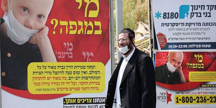 A Haredi man neglects proper mask protocol as he passes a Health Ministry poster in Bnei Brak Health Ministry struggles with obstinate Haredi enclaves as leading rabbi tests positive