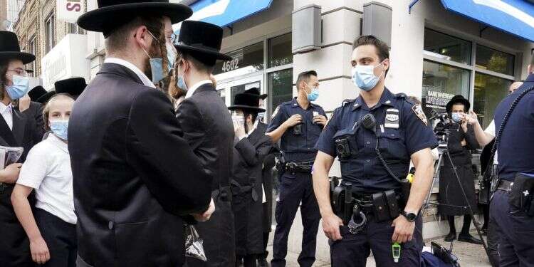 NYPD officer attempts to peacefully disperse a crowd of Jewish Orthodox community members gathering around journalists, Wednesday, Oct. 7, 2020 Turmoil engulfs NY Haredi community amid COVID restrictions, protests