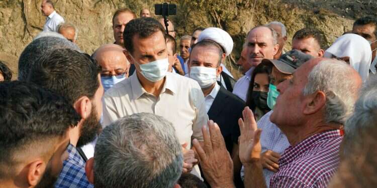 In this photo released Tuesday, Oct. 13, 2020 on the official Facebook page of the Syrian Presidency, Syrian President Bashar Assad, center, wearing a mask to help prevent the spread of the coronavirus, speaks with people during his visit to the coastal province of Latakia, Syria Assad visits areas of western Syria hit by wildfires