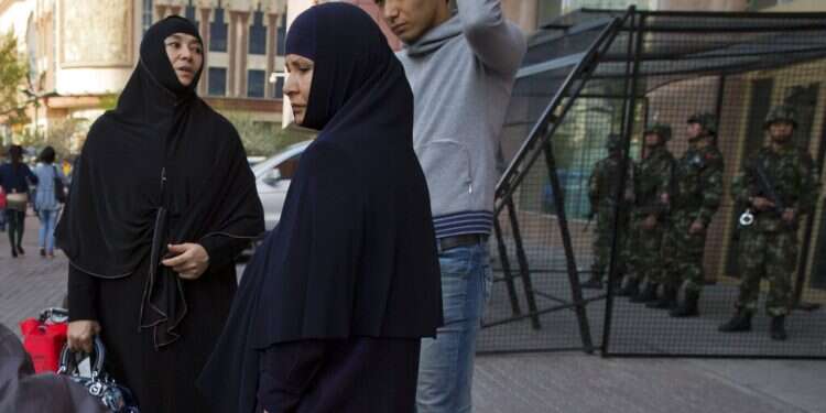 Uighur women stand near a cage protecting heavily armed Chinese paramilitary policemen on duty in Urumqi in China's northwestern region of Xinjiang UN investigator: Minorities' right to worship undermined