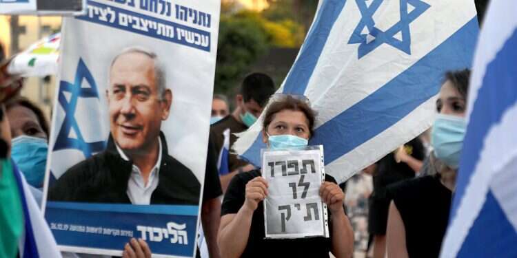 Supporters of Prime Minister Benjamin Netanyahu at a demonstration. The man in the center holds up a sign that reads, 'They cooked up a case' Attorney general to go after corporations in Netanyahu cases