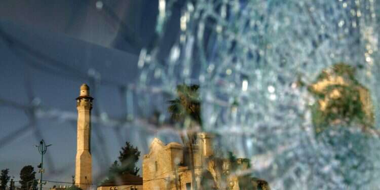 The minaret of the Al-Omari mosque and St. George Greek Orthodox church are reflected in the broken windshield of a vehicle sitting outside a synagogue in the mixed Arab-Jewish town of Lod, central Israel, Wednesday, May 26, 2021 Can riot-stricken mixed city piece together fragile coexistence?