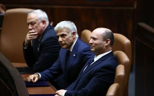 Prime Minister Naftali Bennett, right, sits in the Knesset plenum on Sunday, June 13, 2021, with Blue and White leader Benny Gantz, left, and Yesh Atid leader and Prime MInister-designate Yair Lapid Naftali Bennett sworn in as prime minister after narrow vote of 60:59