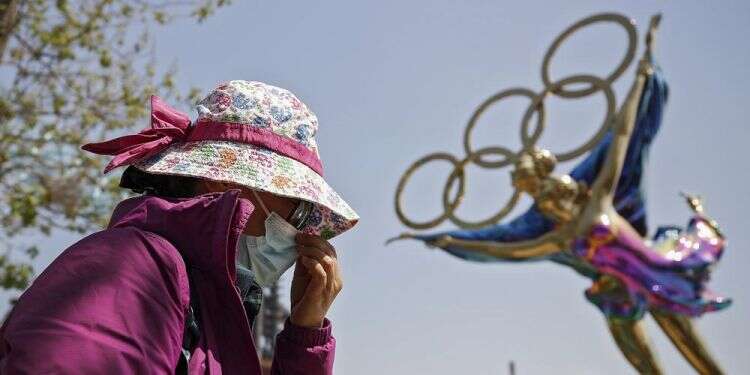 Aa woman adjusts her face mask as she walks by a statue featuring the Beijing Winter Olympics figure skating on display at the Shougang Park in Beijing China keeps virus at bay at high cost ahead of Winter Olympics