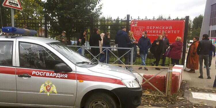 People stand behind the fence near the Perm State University with the a Posguardia (National Guardia) on the left, in Perm, Russia, Sept. 20, 2021 8 dead in shooting at Russian university