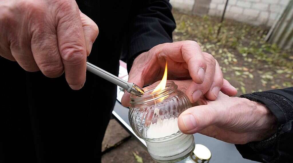 A man helps a person to light a candle to place at a new memorial paying tribute to some 60 Jews executed in the town during the Holocaust in Wojslawice, Poland, on Thursday Oct. 14, 2021. Movement to dedicate unmarked Jewish graves expands through Poland