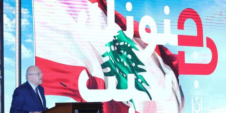 Lebanese PM Najib Mikati speaks as he stands near a slogan that reads 'We love you in your madness' displayed on a screen at the government palace in Beirut, November 4, 2021 Amid turmoil, Lebanon to sell itself to tourists as 'crazy'