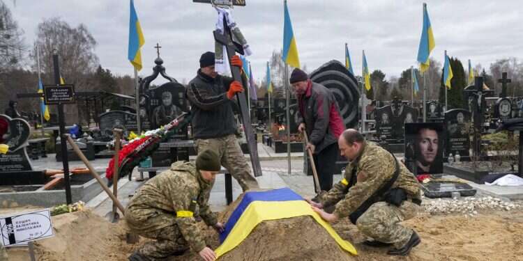 Ukrainian paramedics cover with the National flag the grave of their colleague Valentyna Pushych killed by Russian troops in a cemetery in Kyiv, Ukraine, Saturday, March 5, 2022 As ceasefire collapses, IAEA voices concern over state of nuclear facilities