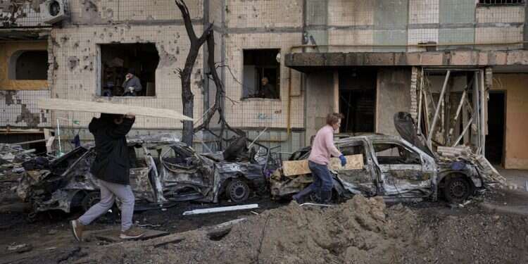 People carry wooden boards to cover the windows of a building damaged by a bombing the previous day in Kyiv, March 21, 2022 Ukrainian forces holding Mariupol, Zelenskyy reports 'step by step' progress in talks