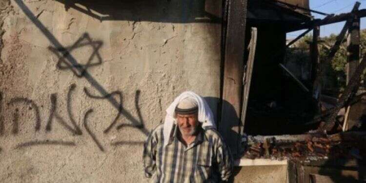A Palestinian man stands next to graffiti reading 'Revenge' n the West Bank village of Doma, July 31, 2015 Security escalation prompts uptick in 'price tag' incidents
