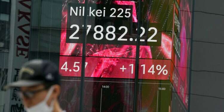 A person wearing a protective mask walks in front of an electronic stock board showing Japan's Nikkei 225 index at a securities firm, Sept. 20, 2022, in Tokyo Asia shares rise on US rally ahead of expected Fed rate hike