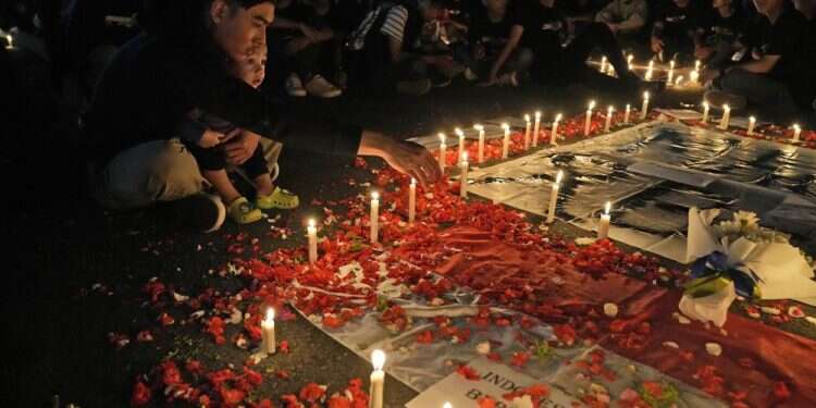 A man sprinkles flowers during a candle light vigil for the victims of Saturday's soccer riots, in Jakarta, Indonesia, Oct. 2, 2022 125 dead after tear gas triggers crush at Indonesia soccer match
