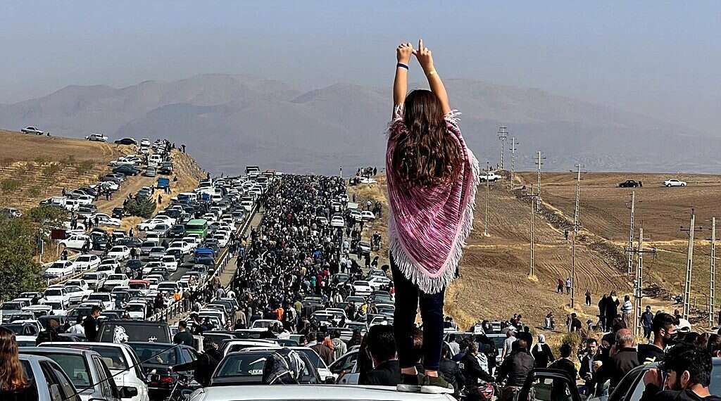 An unveiled woman standing on top of a vehicle as thousands make their way towards Aichi cemetery in Saqez, Mahsa Amini's hometown, posted on Twitter on Oct. 26, 2022 Condemnations pour in as Iran executes karate champion for protesting