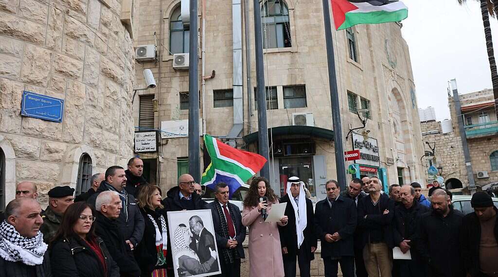 A Palestinian man holds a portrait of late Palestine Liberation Organization (PLO) leader Yasser Arafat and South Africa's anti-apartheid icon Nelson Mandela before raising the South African national flag outside the municipality building in Bethlehem South Africa's hate toward Israel, explained