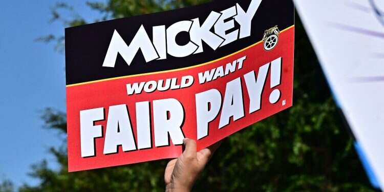 A Disney employee holds up a sign during a rally outside the main entrance of Disneyland Resort in Anaheim, California, July 17, 2024, ahead of a planned strike authorization vote Disneyland workers poised to strike amid contract disputes