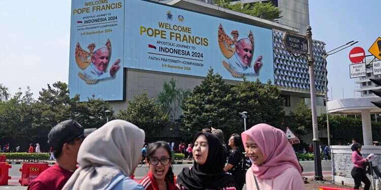 Muslim women chat as a large digital advertisement board with a welcoming message for Pope Francis is displayed on the facade of a building nearby in Jakarta, Sunday, Sept. 1, 2024, ahead of his visit to Indonesia from Sept. 3-6 Pope Francis to visit Indonesian mosque for religious harmony