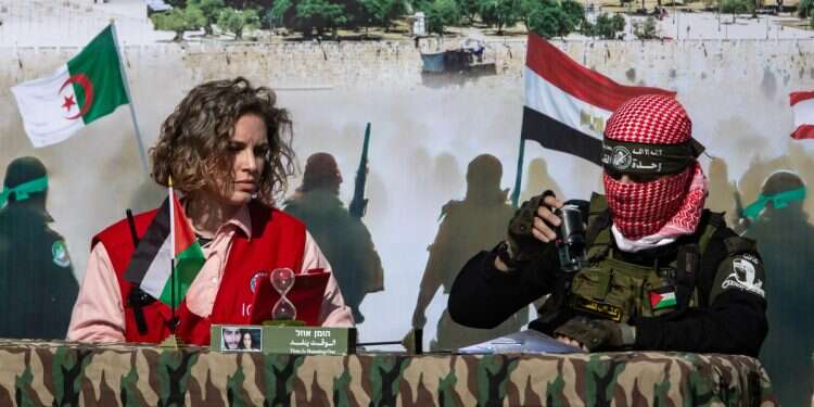 A Red Cross representative and a terrorist from Hamas's Izz ad-Din al-Qassam Brigades exchange handover certificates of three Israeli hostages during their release ceremony, in Khan Yunis, southern Gaza Strip, 15 February, 2025 Jewish suffering is repackaged for political consumption