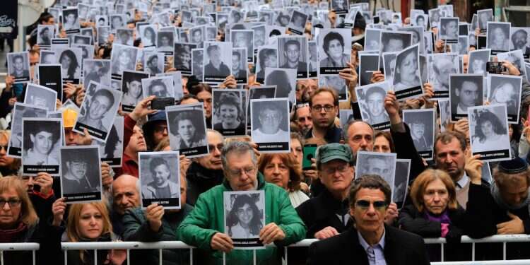 People holding pictures of victims of the 1994 bombing attack against the Argentine Israelite Mutual Association (AMIA) Jewish community center that killed 85 people and injured 300, during the commemoration of the attack's 25th anniversary, in Buenos Aires on July 18, 2019 Argentina demands arrest warrant for Khamenei