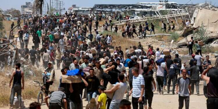 People walk as Palestinians receive aid supplies from the US-backed Gaza Humanitarian Foundation, near Netzarim corridor, May 29, 2025 Gaza is not a concentration camp