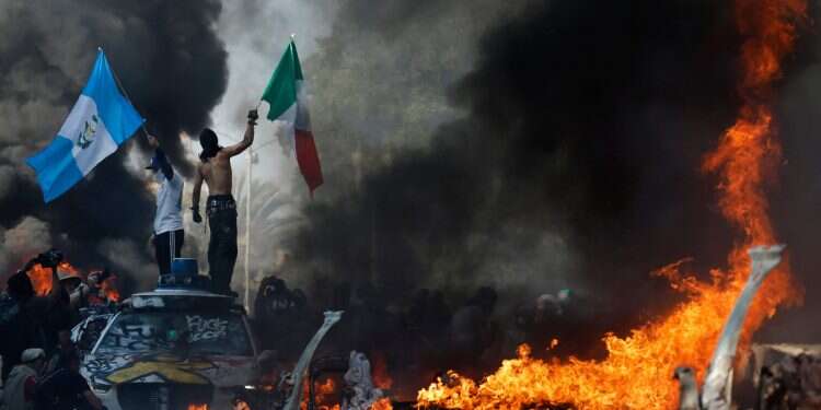 Protestors wave flags as burning and vandalized Waymo cars line the street on June 8, 2025 in Los Angeles, California LA riots rage as Trump deploys troops without governor consent