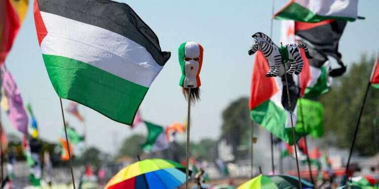 Revellers hold up a Palestinian flag, a prop head wearing a balaclava in the colours of the Irish flag, and a representation of a zebra, on the day Kneecap performs at Glastonbury Festival at Worthy Farm in Pilton, Somerset, Britain, June 28, 2025 Irish band banned from popular music festival over Hamas praise