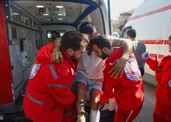 Red Crescent workers carry a wounded man outside the Russian air base in Hmeimim, near Latakia in Syria's coastal region on March 11, 2025, as they evacuate wounded members of the Alawite sect who have sought refuge there following recent violence and revenge killings Alawite homes marked with X's; forced evacuation from Damascus