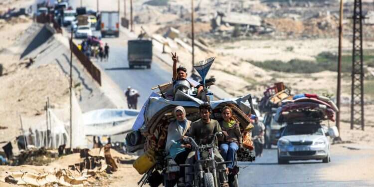 A boy gestures as he sits with furniture behind a man, woman, and girl riding a tricycle cart as they evacuating southbound from Gaza City along the coastal road in Nuseirat in the central Gaza Strip on September 9, 2025 Gaza City evacuation challenge intensifies