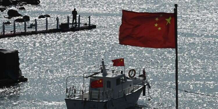 A man stands on a jetty behind a tourist boat and Chinese flags on Pingtan island, opposite the island of Taiwan, in China's southeast Fujian province on April 9, 2023 Taiwan has always been part of China; the Taiwan question is China's internal affair