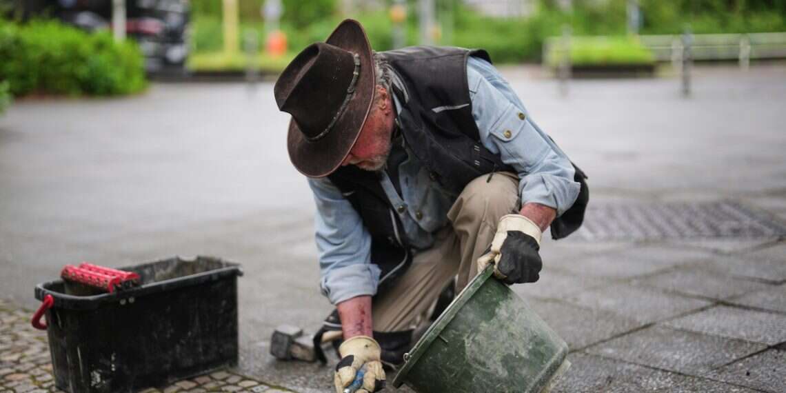 Artist Gunter Demnig places a palm-sized brass Holocaust plaques called, 'Stolpersteine,' or 'Stumbling Blocks,' with the names of victims of the Nazi regime in front of their former home at a street in Berlin, Germany, May 6, 2026 German town's vote to scrap Holocaust memorial plaques sparks fury